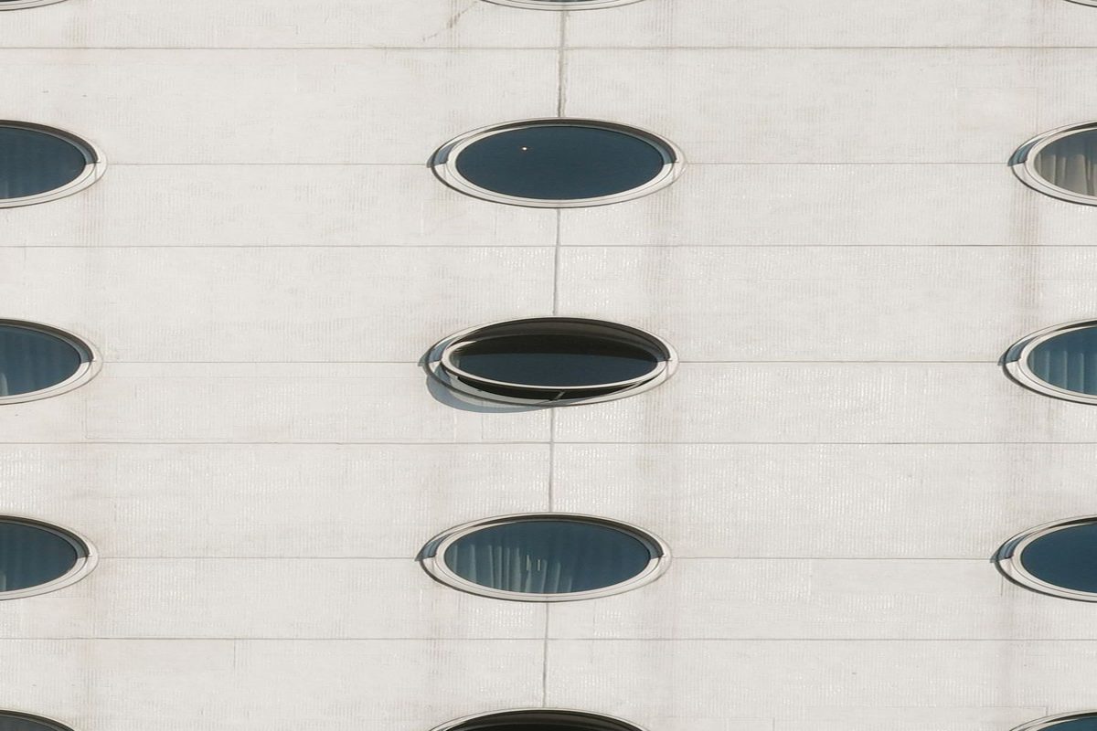 Fachada de ventanas circulares en grilla, con una sola ventana entreabierta en un ángulo distinto a las demás: la posición de un punto que se desvía del resto se detecta de inmediato, sin necesitar barras