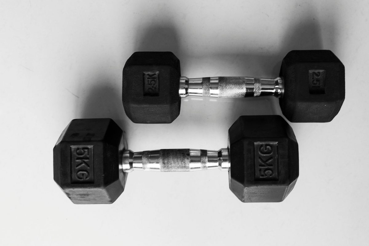 Dos mancuernas de gimnasio en blanco y negro, cada una con dos discos octogonales unidos por una barra: la misma forma exacta de un dumbbell chart — dos puntos conectados por una línea, de donde el gráfico toma su nombre