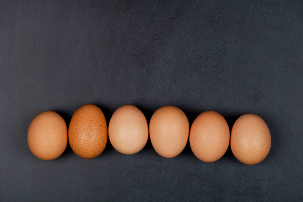 Seis huevos reales del mismo tipo y tamaño alineados en una fila sobre fondo oscuro, sin marca ni etiqueta: la misma lógica de un pictogram chart, donde una cantidad se representa repitiendo la misma unidad fija, nunca agrandando una sola unidad