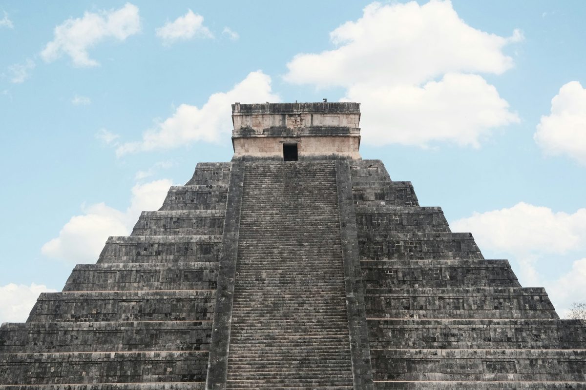 Pirámide escalonada de piedra vista desde abajo, con una base ancha que se angosta en niveles simétricos hacia la cima: la misma silueta que lee una pirámide poblacional, donde el ancho de cada nivel —no un punto ni una línea— es lo que comunica la estructura