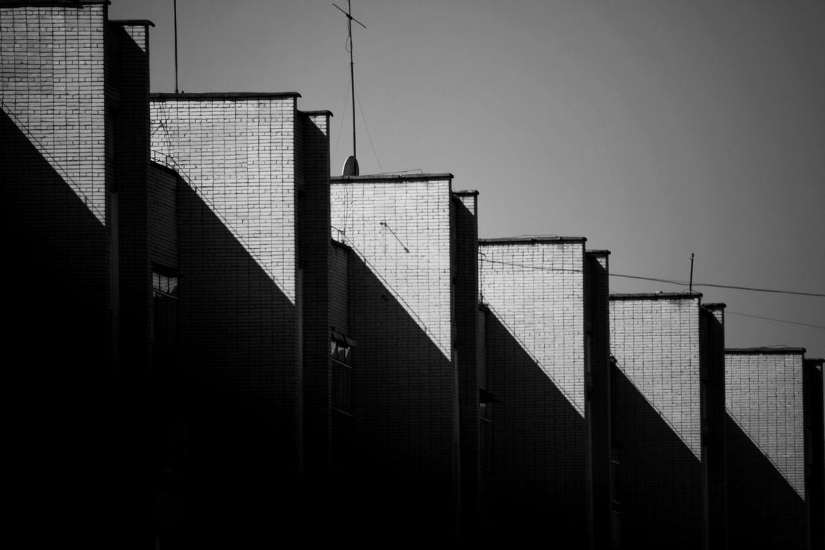 Fachadas de ladrillo en blanco y negro, escalonadas en altura, unidas por una sola línea diagonal de luz que cruza todas sus cimas: la misma lógica de un waterfall chart — bloques separados que no nacen todos del mismo nivel, conectados por una línea continua que guía el ojo de uno al siguiente